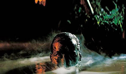 Still from "Apocalypse Now" showing Captain Willard with camouflaged face rising from swampy water